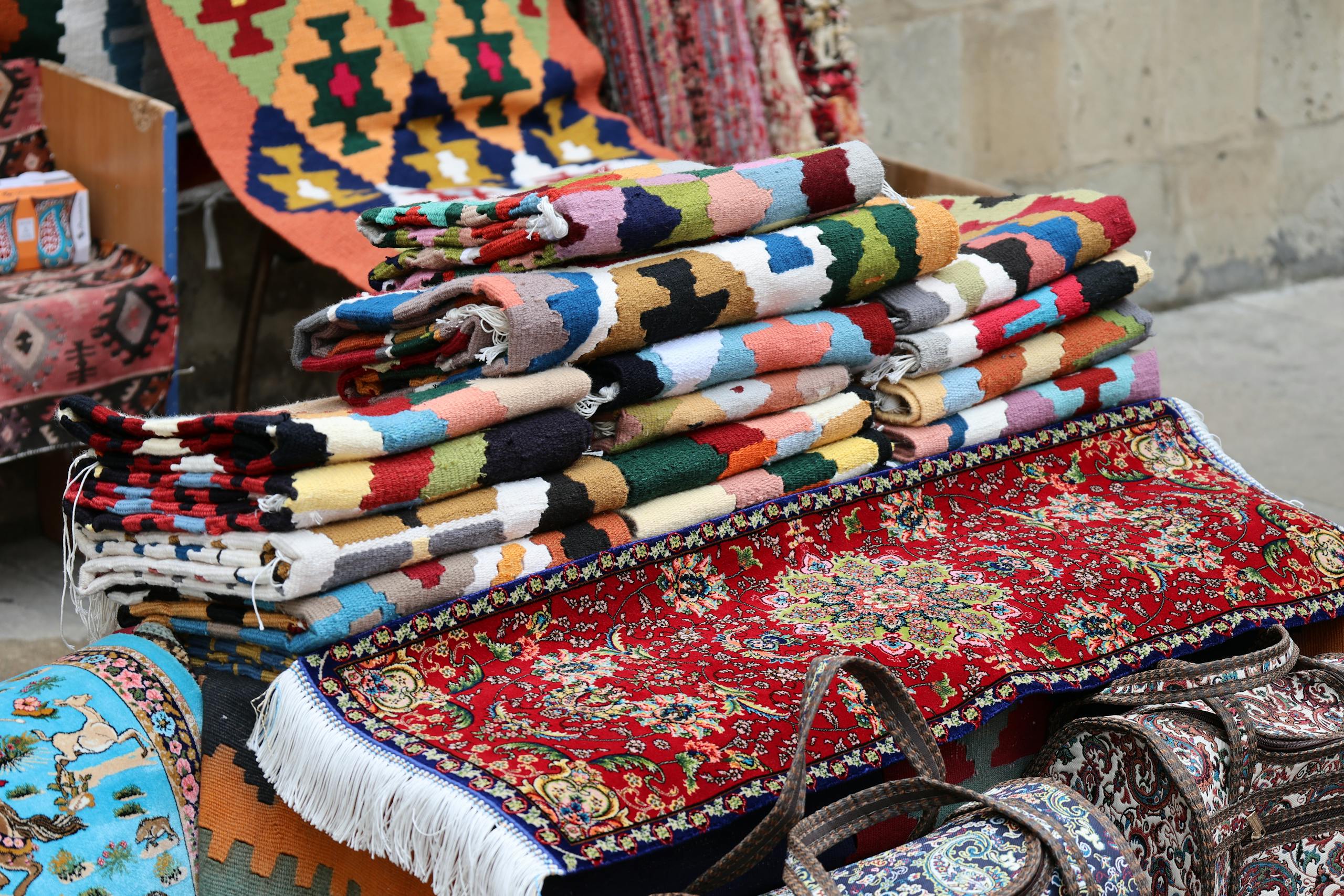 Vibrant and diverse traditional woven rugs displayed in an outdoor market setting.
