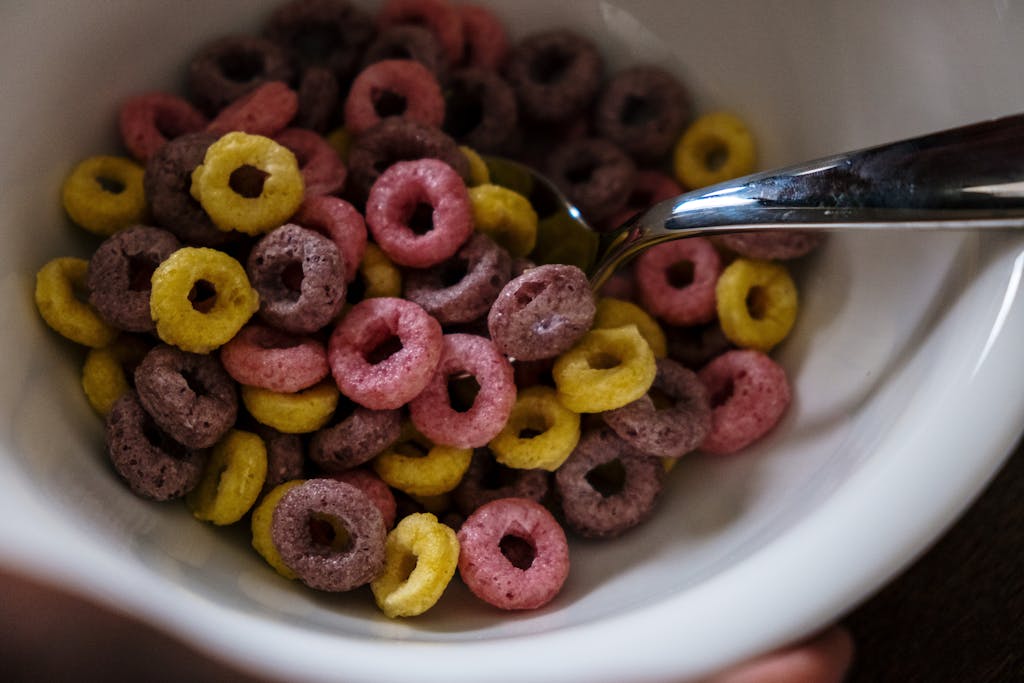 Vibrant fruity cereal rings in a white bowl with a spoon, emphasizing breakfast theme.