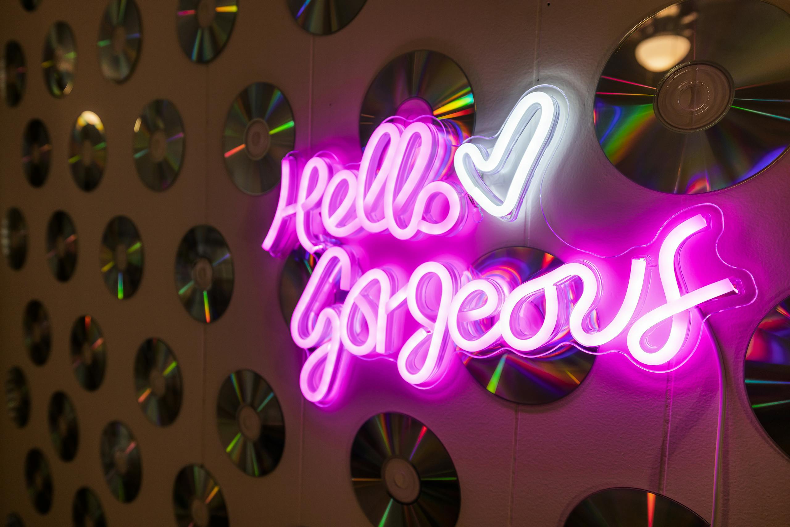 Vibrant neon sign saying 'Hello Gorgeous' with CDs reflecting colorful lights.