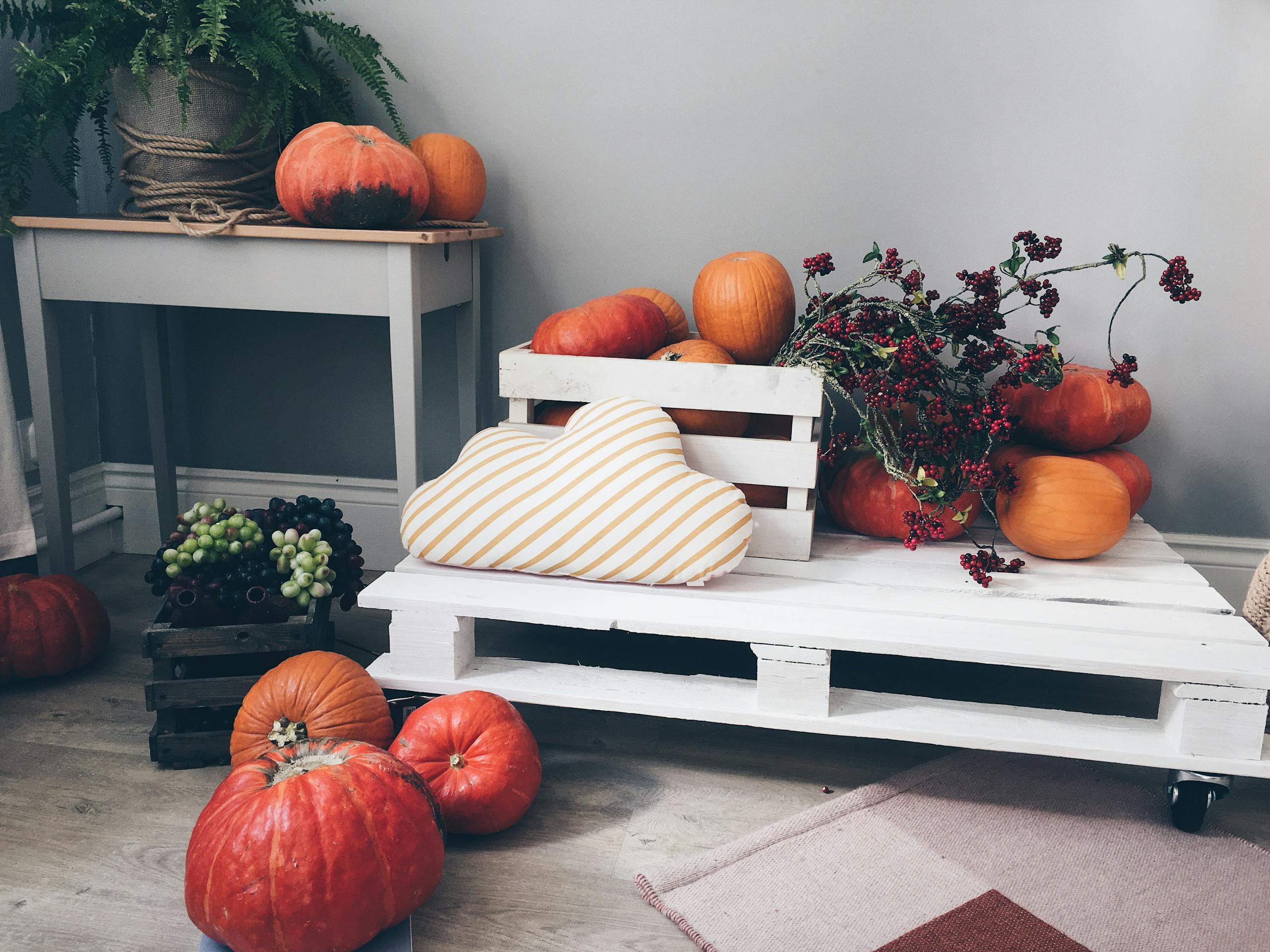 Warm autumn arrangement indoors with pumpkins, berries, and cozy decor on wooden pallets.