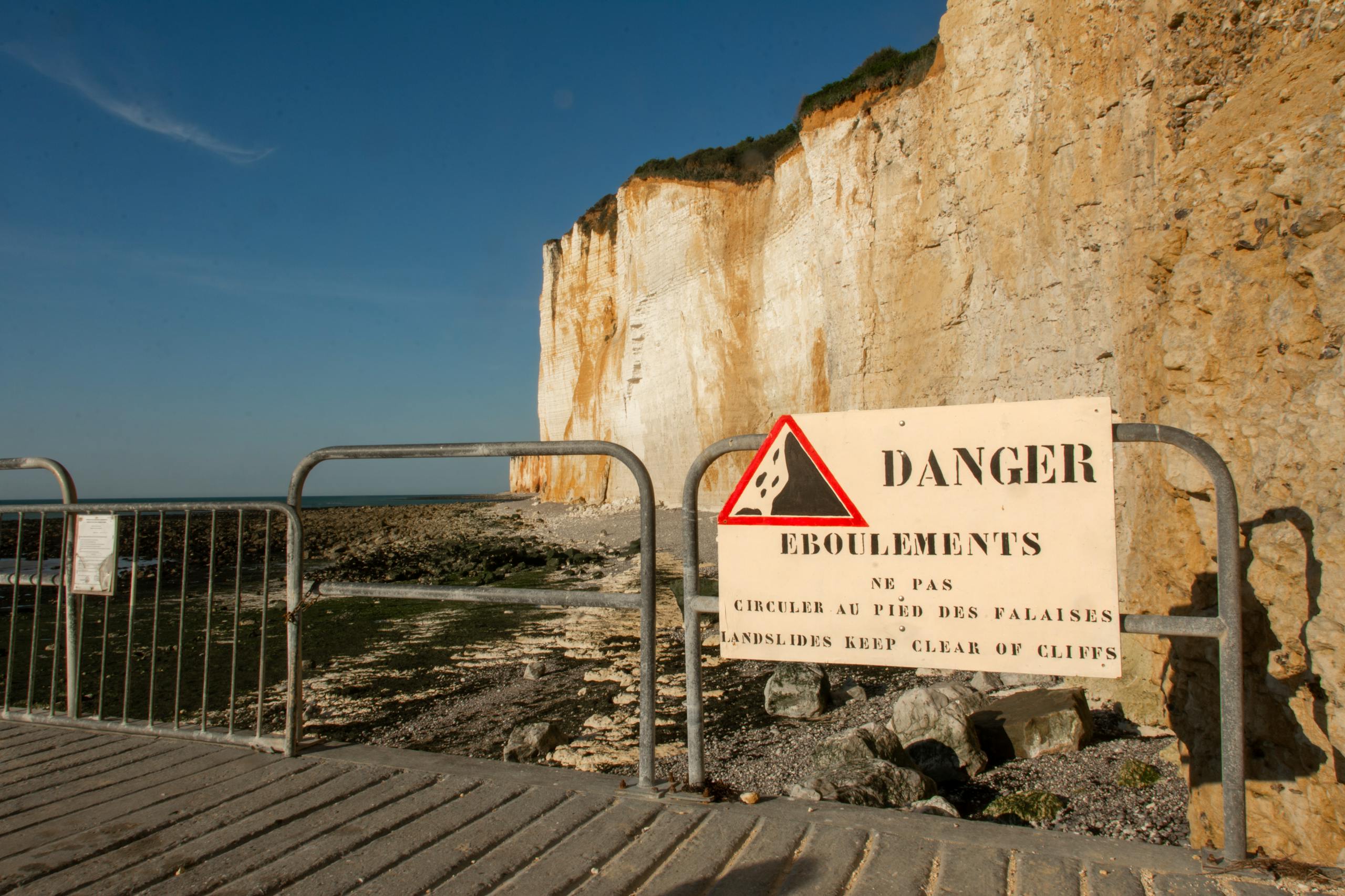 Warning sign by cliffs in France indicating danger of falling stones. Clear view of natural landscape.