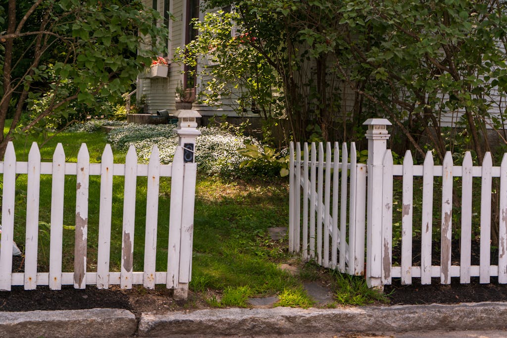 White picket fence in a lush garden setting beside a traditional house.
