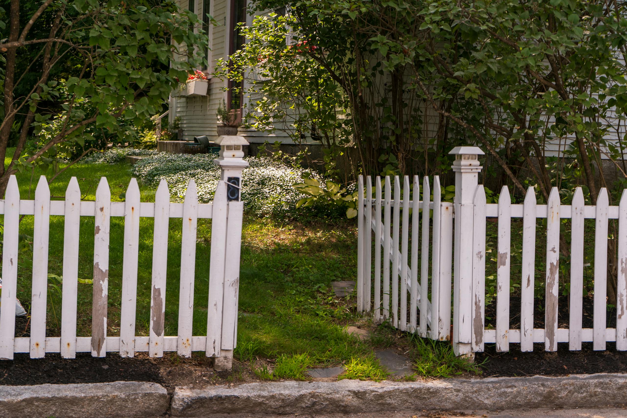 White picket fence in a lush garden setting beside a traditional house.