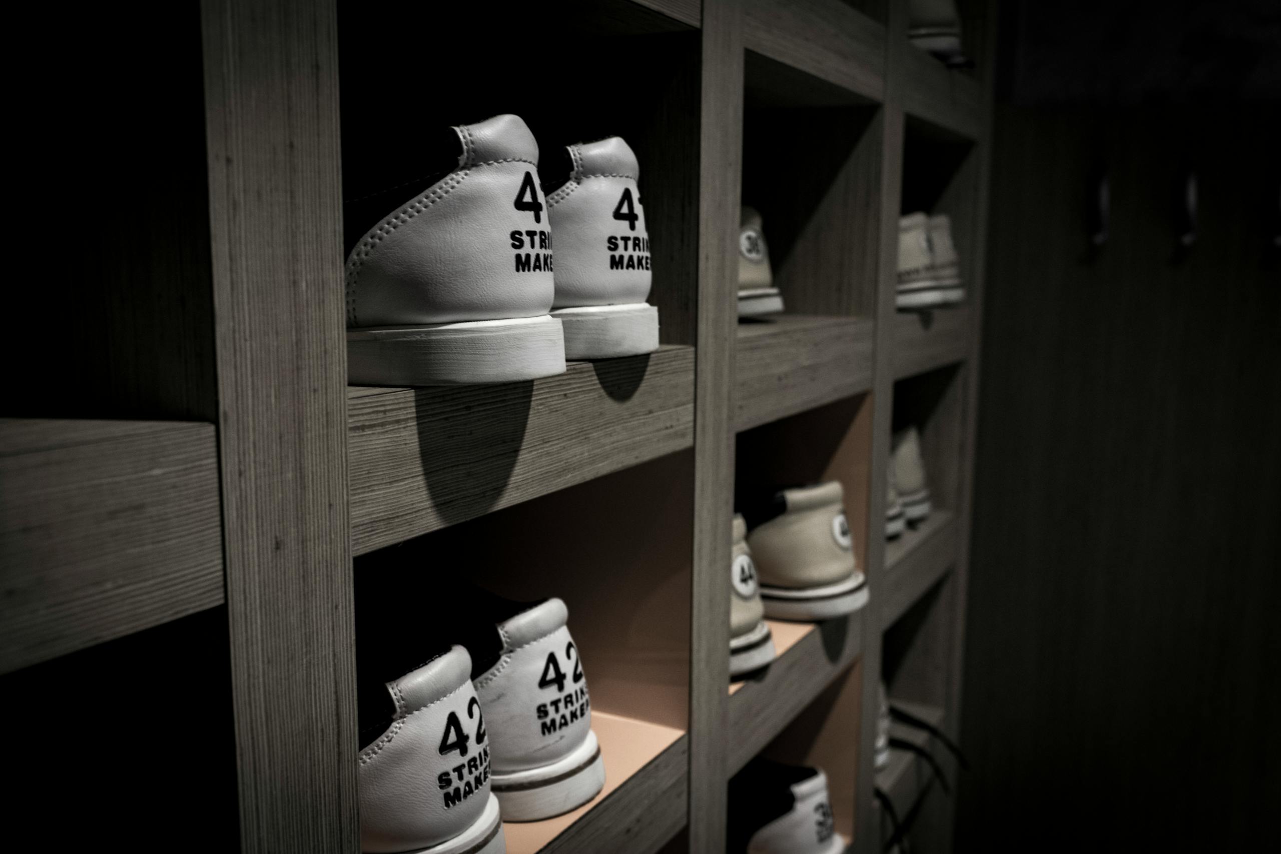 White sneakers labeled with '42' are neatly organized on wooden shelves in a dimly lit room.