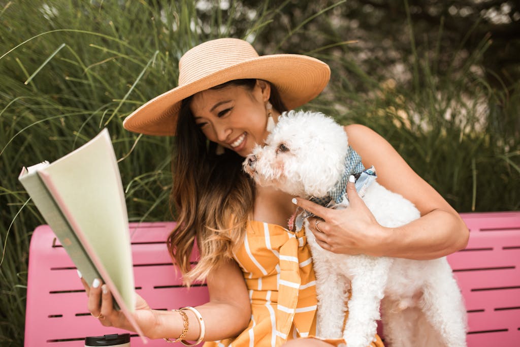 Woman enjoys a summer day reading with her dog on a pink park bench surrounded by greenery.