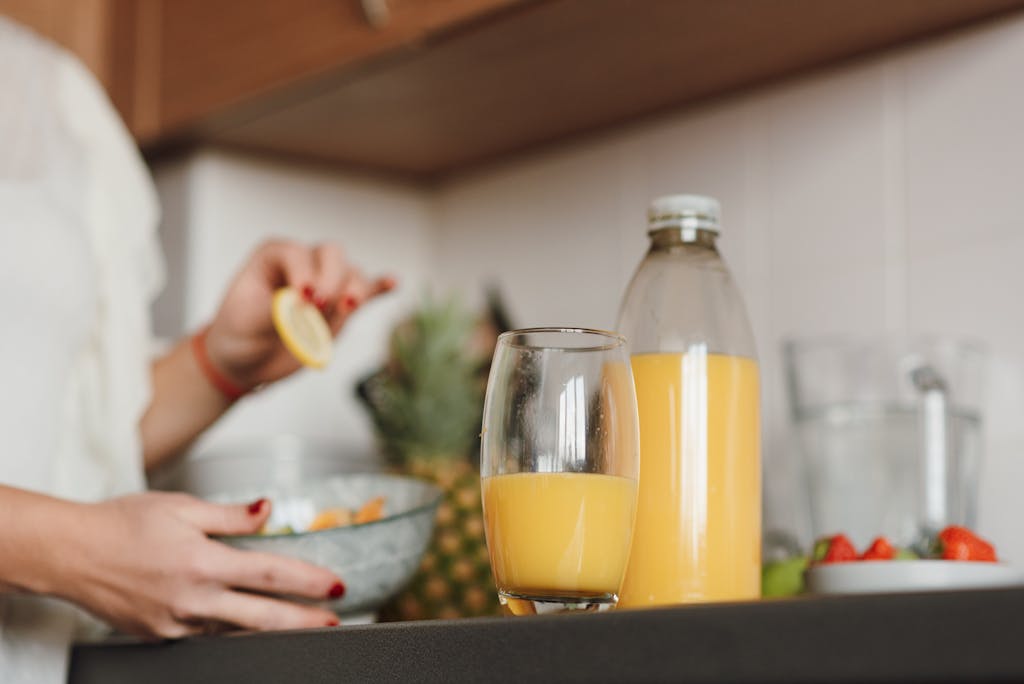 Woman preparing fresh citrus juice in a modern kitchen setting with fruits and glass bottle.