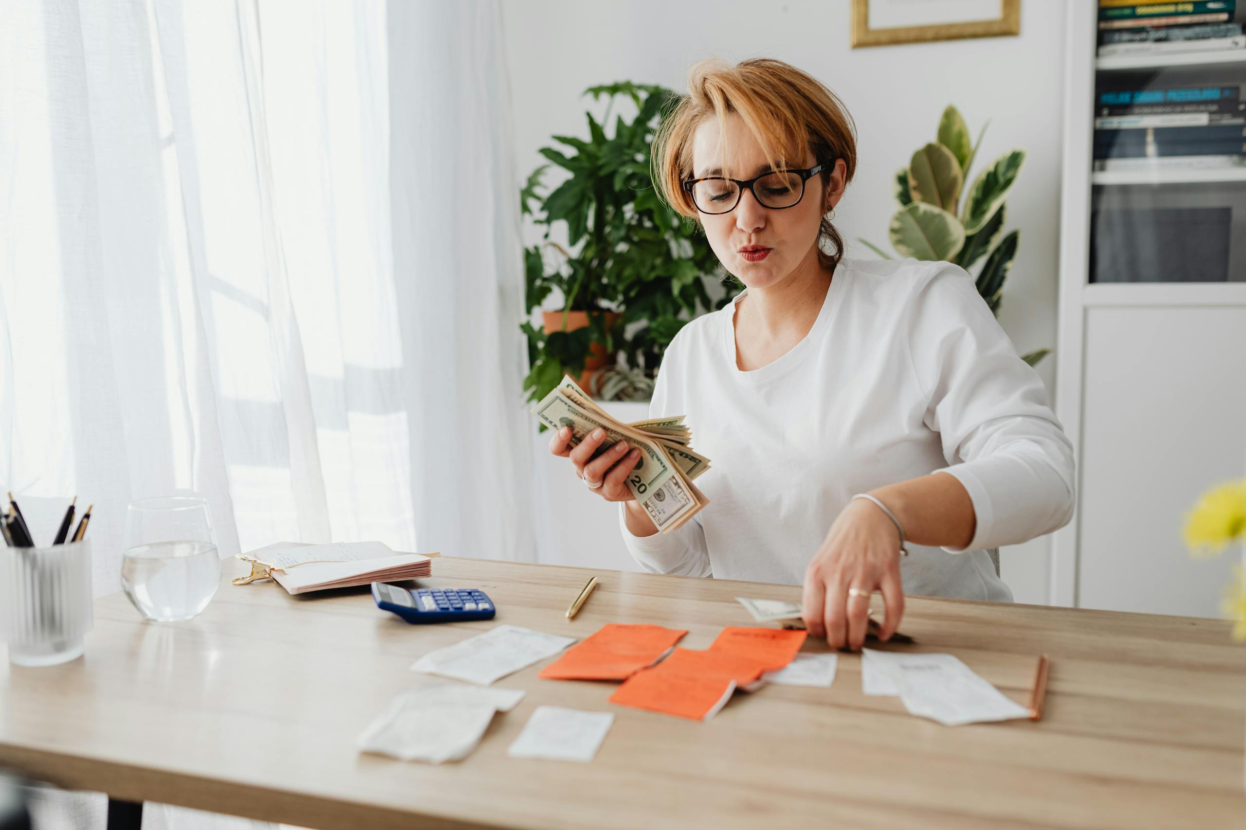 Woman sitting at a table counting cash and organizing receipts with a calculator nearby.