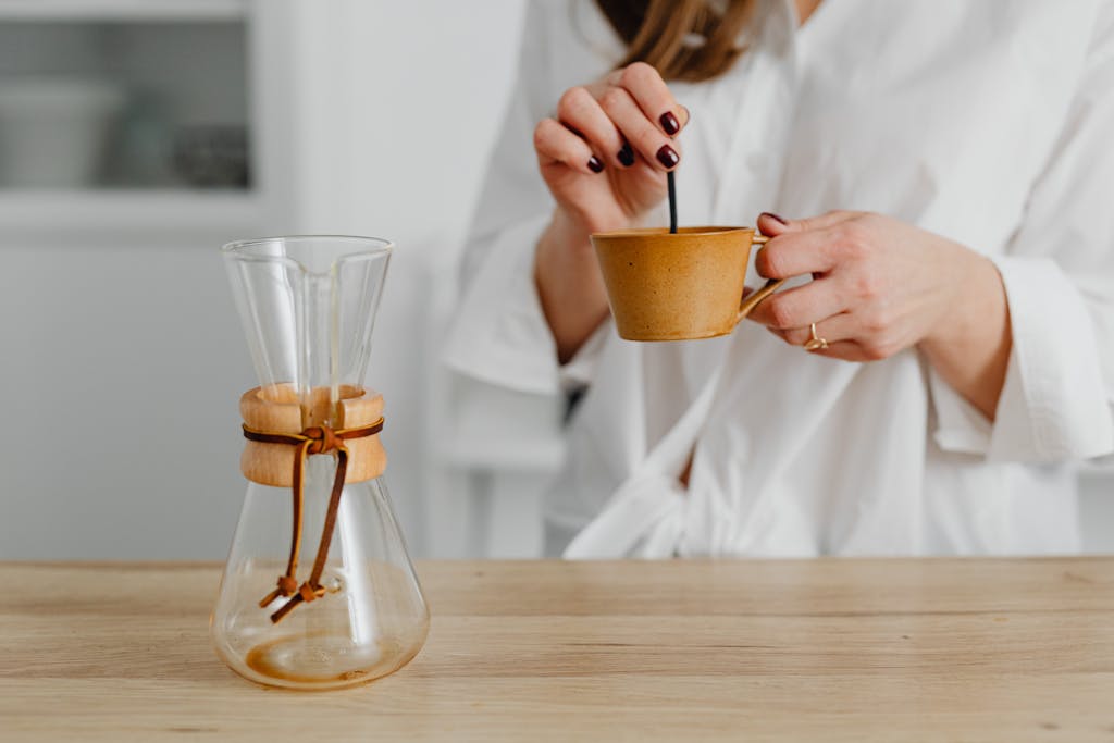 You Might Be Smelling Bad Because of These 10 Common Foods 4 Woman stirring coffee in ceramic cup beside blank Chemex on wood table.
