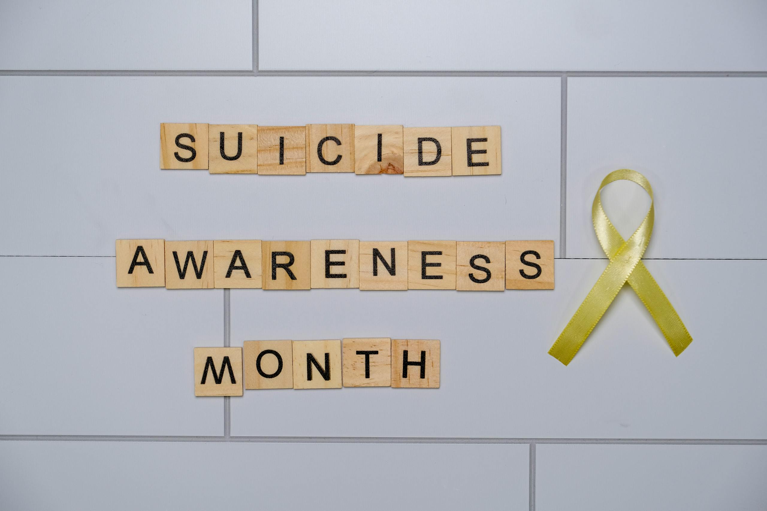 Wooden blocks spelling 'Suicide Awareness Month' with a yellow ribbon.