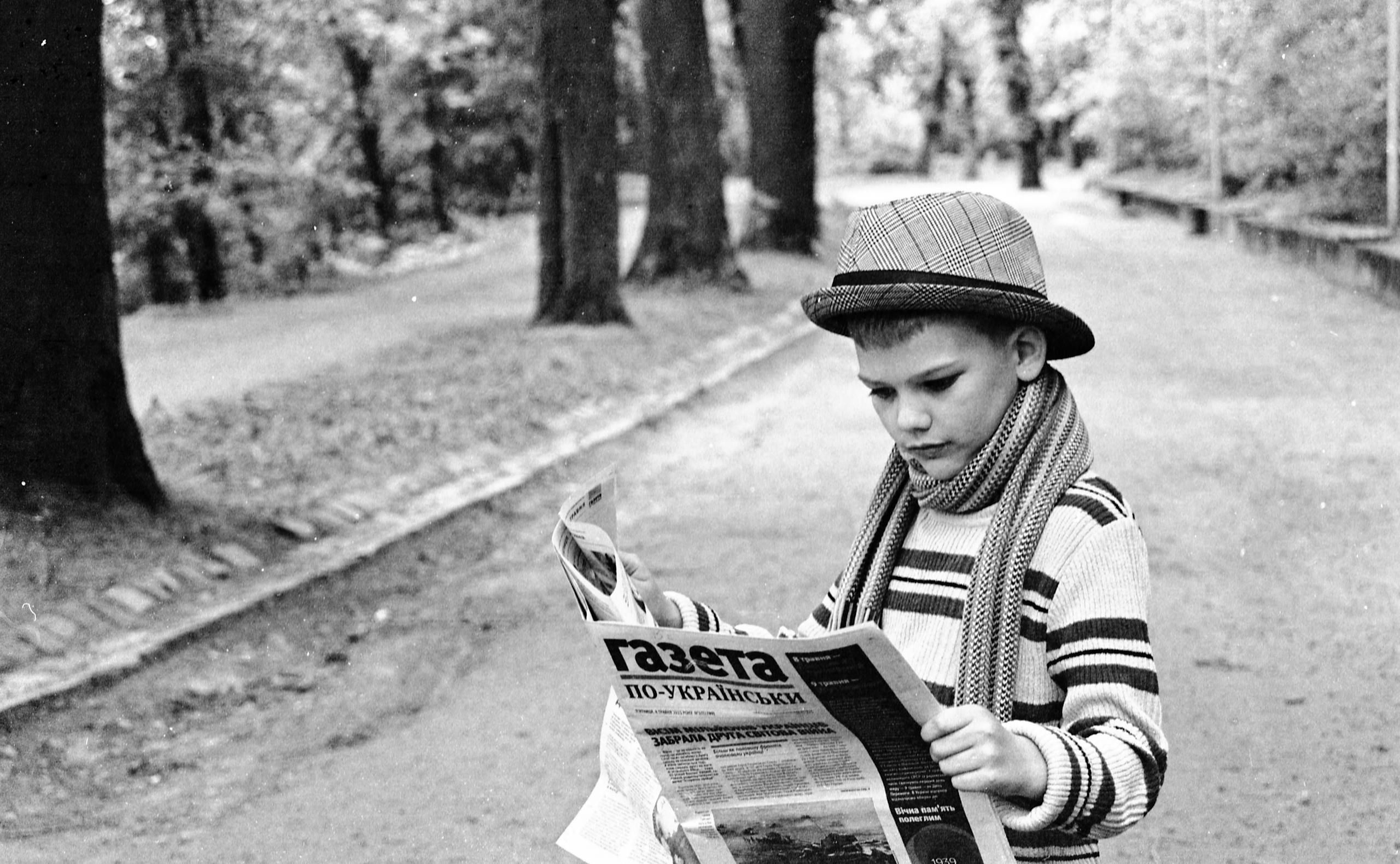 Young boy in vintage attire reading a Ukrainian newspaper in a Lviv park.