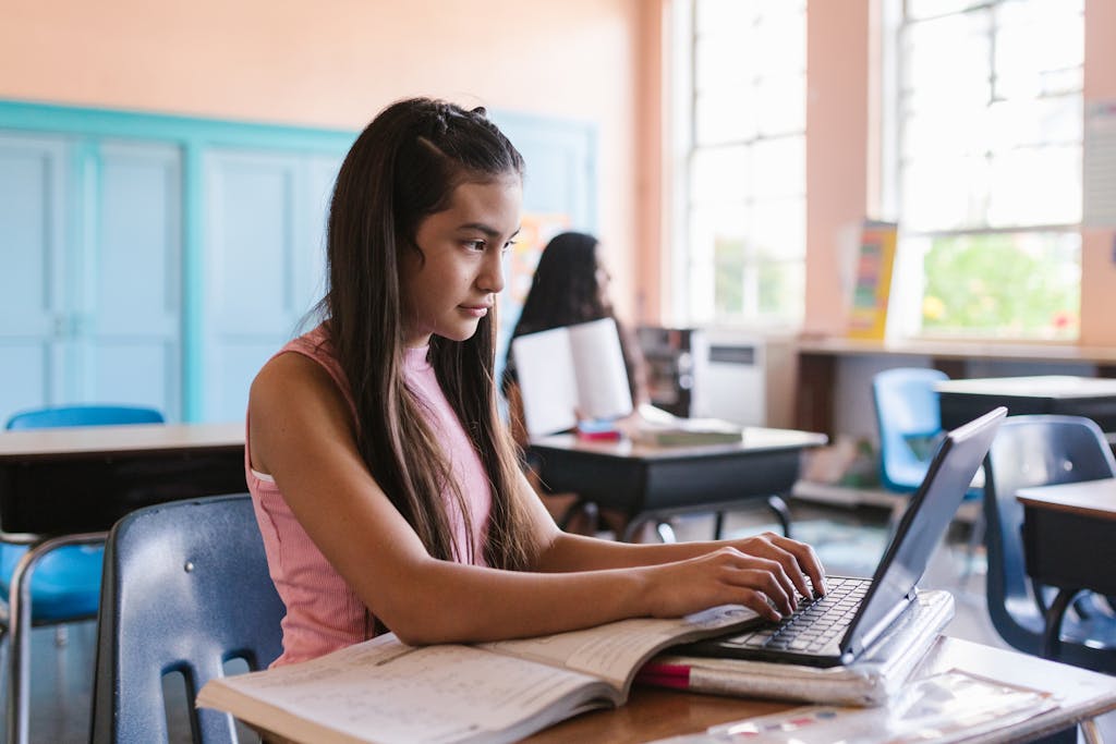 Young girl engaged with a laptop in a classroom environment, illustrating focused learning.