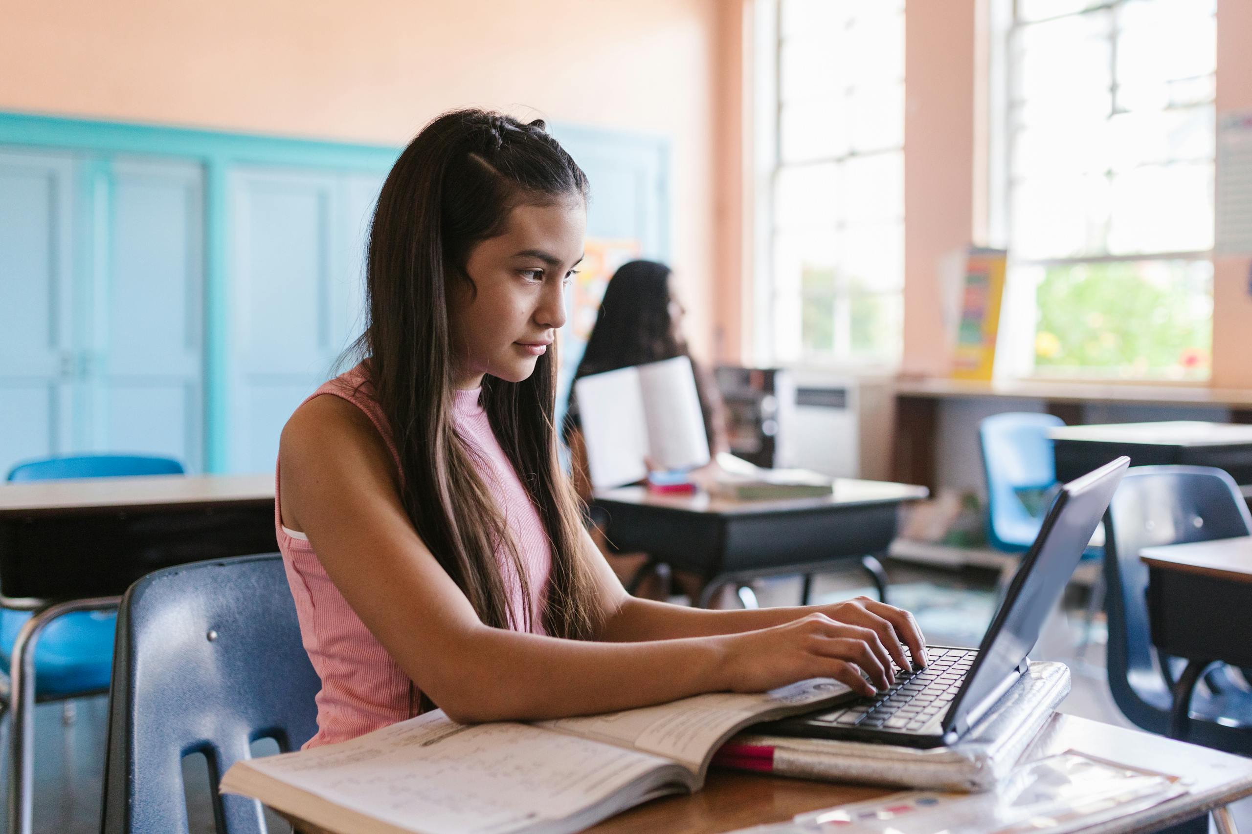 Young girl engaged with a laptop in a classroom environment, illustrating focused learning.