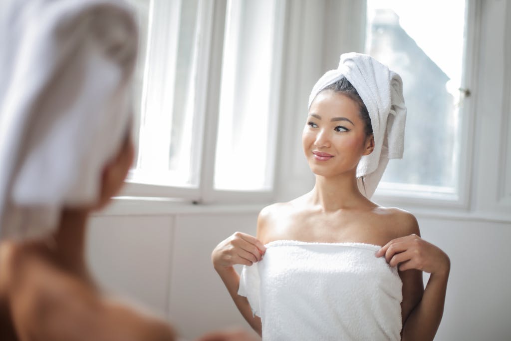 Ignore These 8 Hacks and Your Mornings Will Turn Chaotic and Stressful 2 Young woman enjoying a cozy bath moment with a towel in a bright bathroom, reflecting happiness.