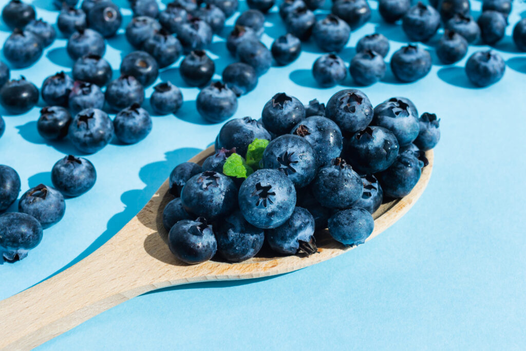 Blueberries in a wooden spoon on blue background. Closeup overview. Fresh sweet, tasty cooking ingredient. Ripe healthy summer snack. Organic raw vegan dessert food. Banner frame design template