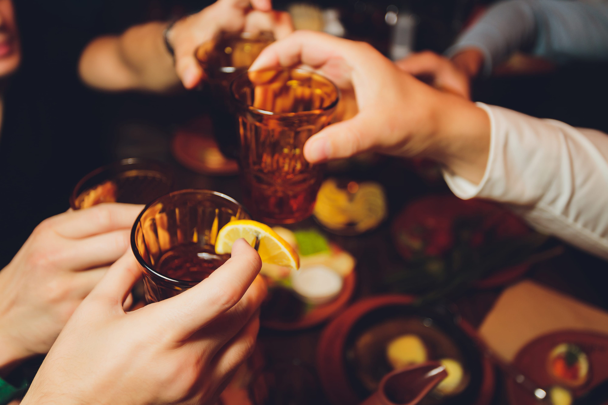 Close up shot of group of people clinking glasses with wine or champagne in front of bokeh background. older people hands.