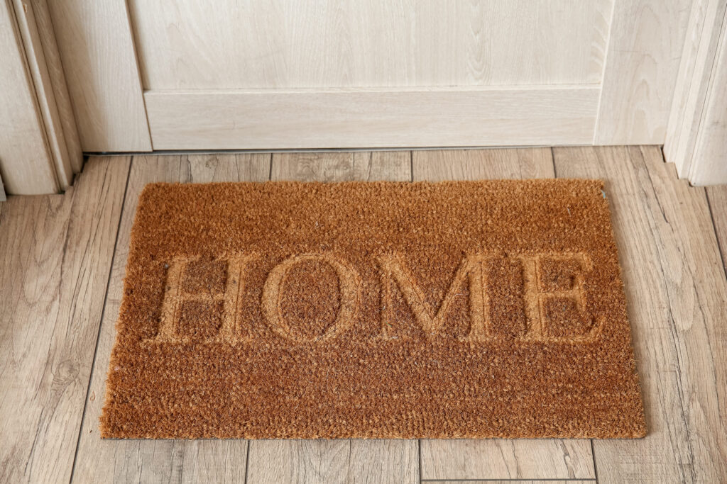 Mat with word HOME near wooden door in hallway