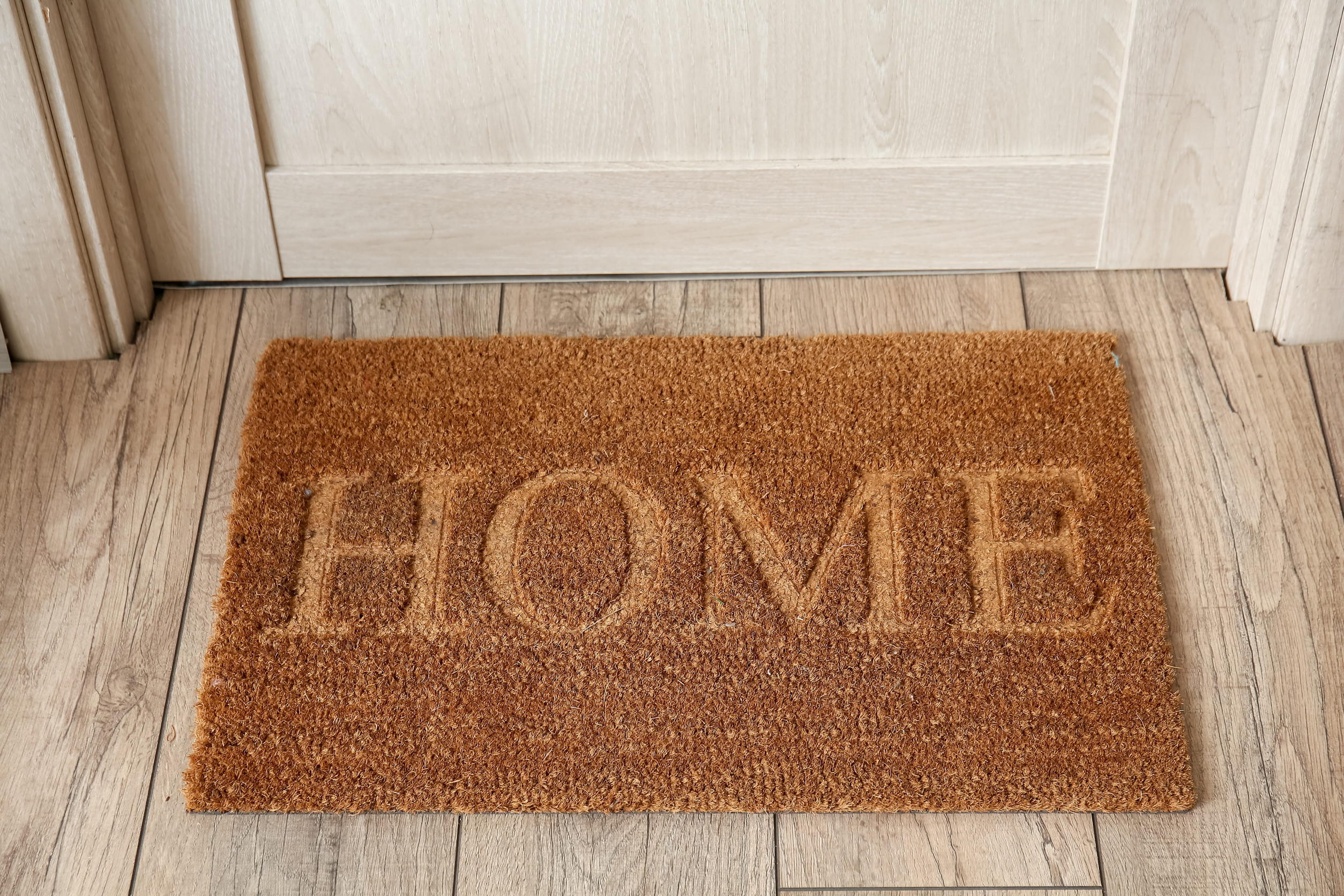 Mat with word HOME near wooden door in hallway