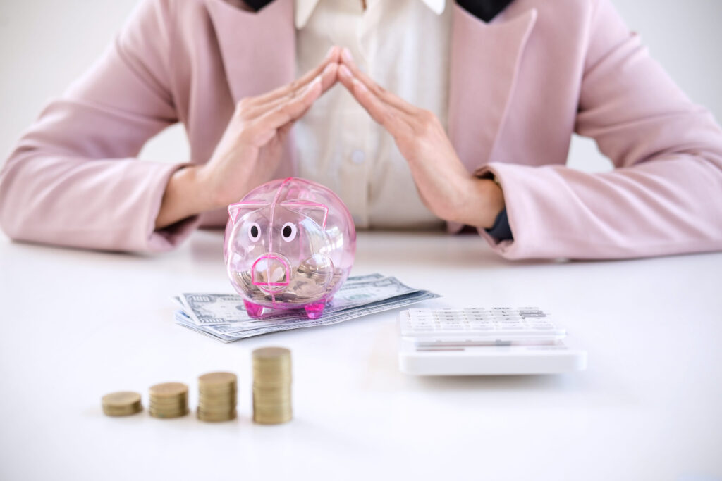 Business woman saving coins into piggy bank and using calculator to analysis business investment strategy with income of money coin and dollar, financial concept.