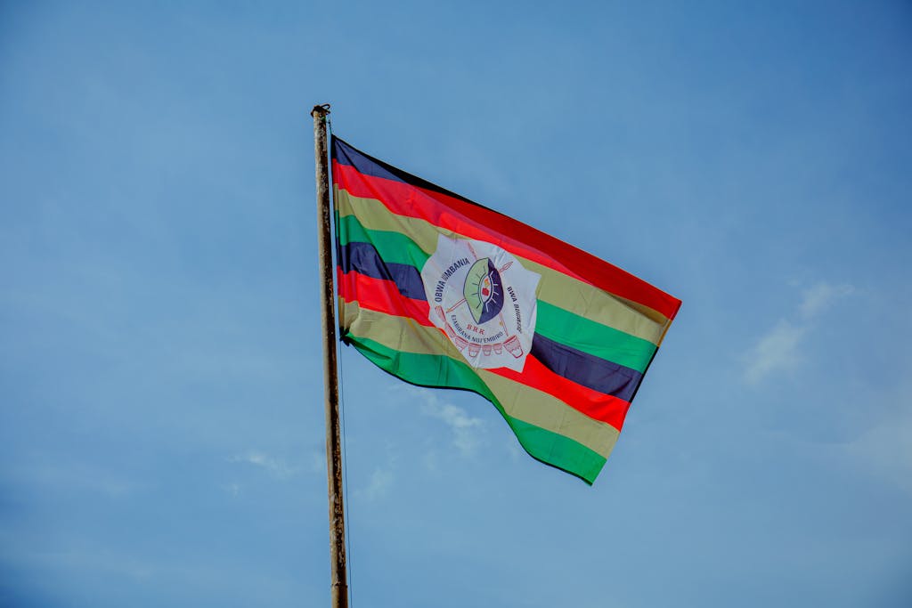 A colorful flag with stripes and emblem waving in the clear blue sky, symbolizing pride.