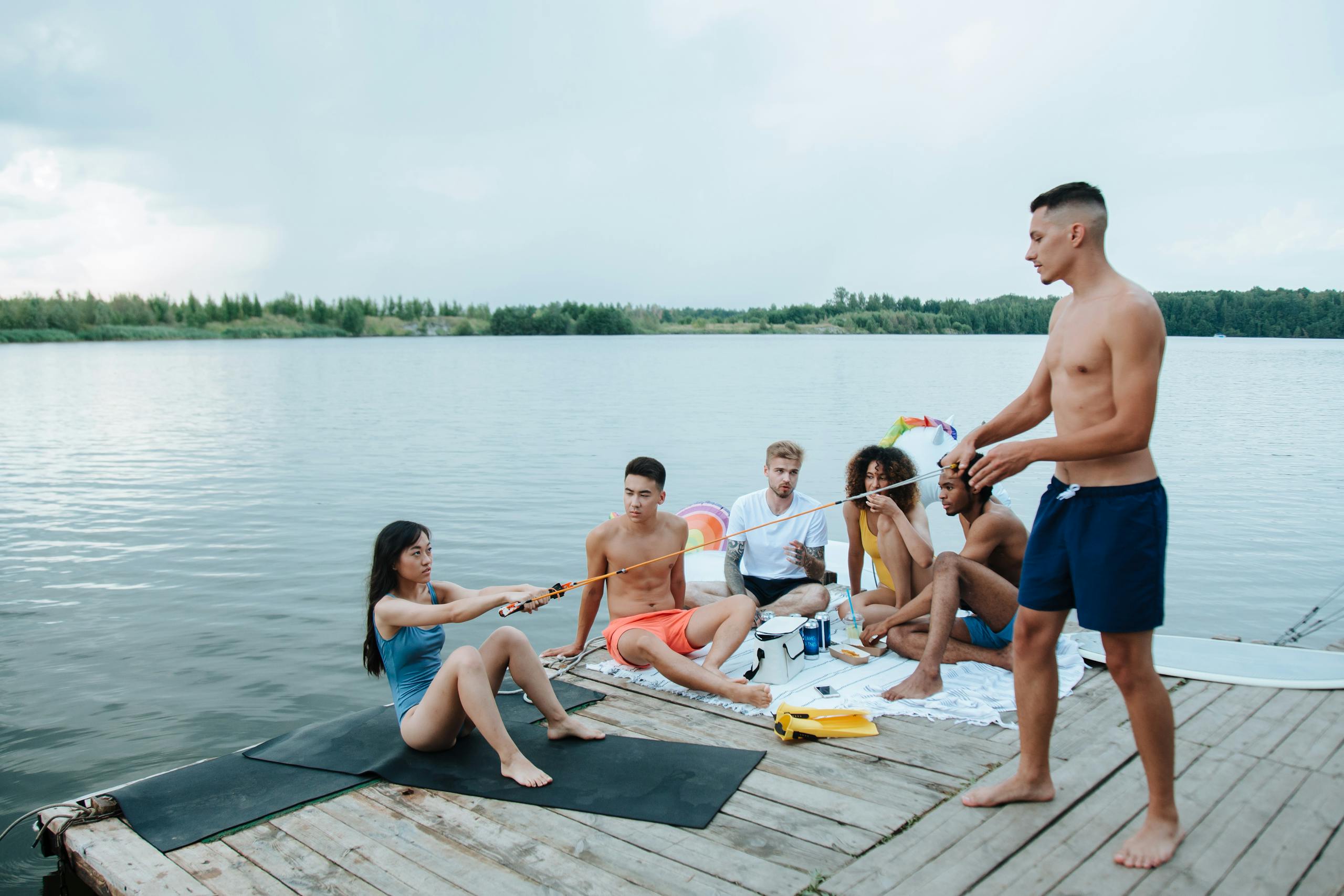 A diverse group of friends enjoys a summer day socializing by the lake on a wooden pier.