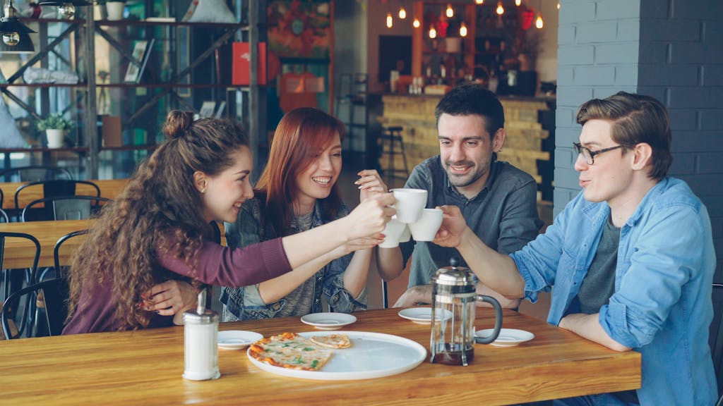 A group of friends toasting with coffee cups at a cozy café setting.