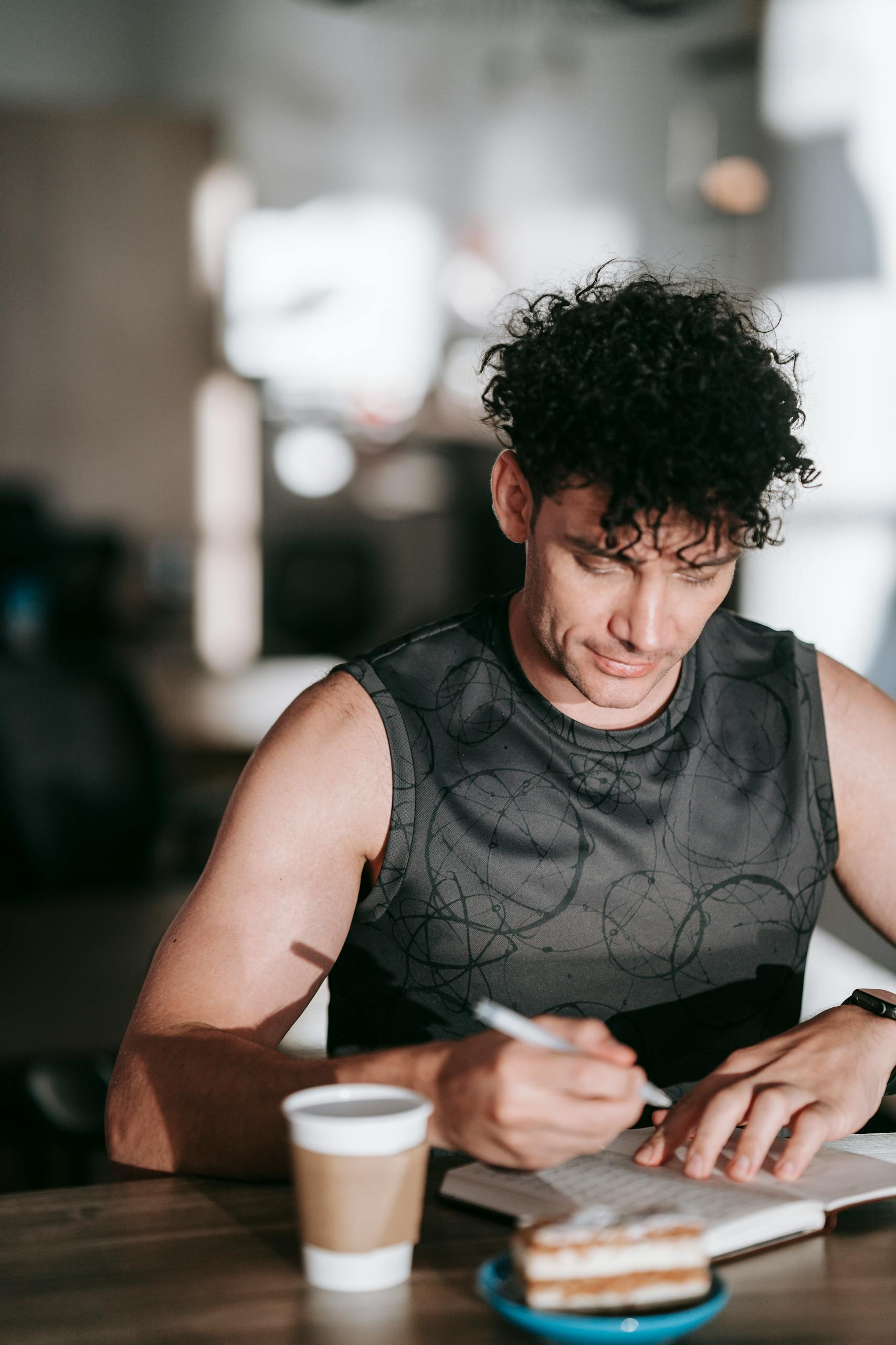 A man in activewear writing in a journal, enjoying coffee indoors.