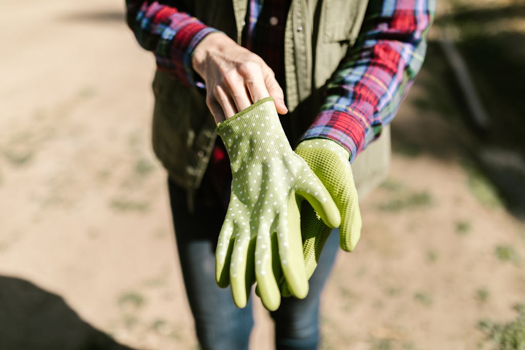 A person in casual attire putting on green polka-dotted garden gloves under sunlight.
