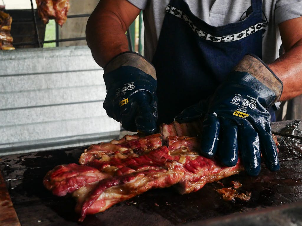 A person preparing traditional BBQ meat with gloves in Uribelarrea, capturing authentic Argentine cuisine.