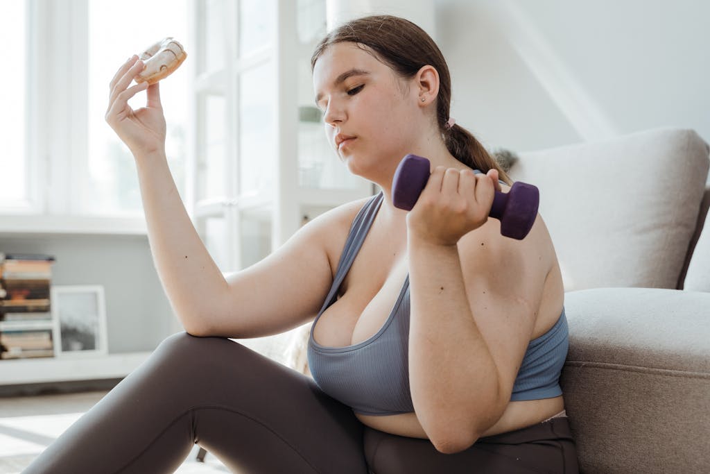 A plus size woman in activewear balancing a dumbbell and a donut, symbolizing fitness and indulgence.