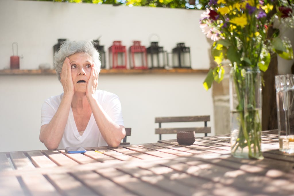 A senior woman with gray hair looking shocked outdoors at a patio table in Portugal.
