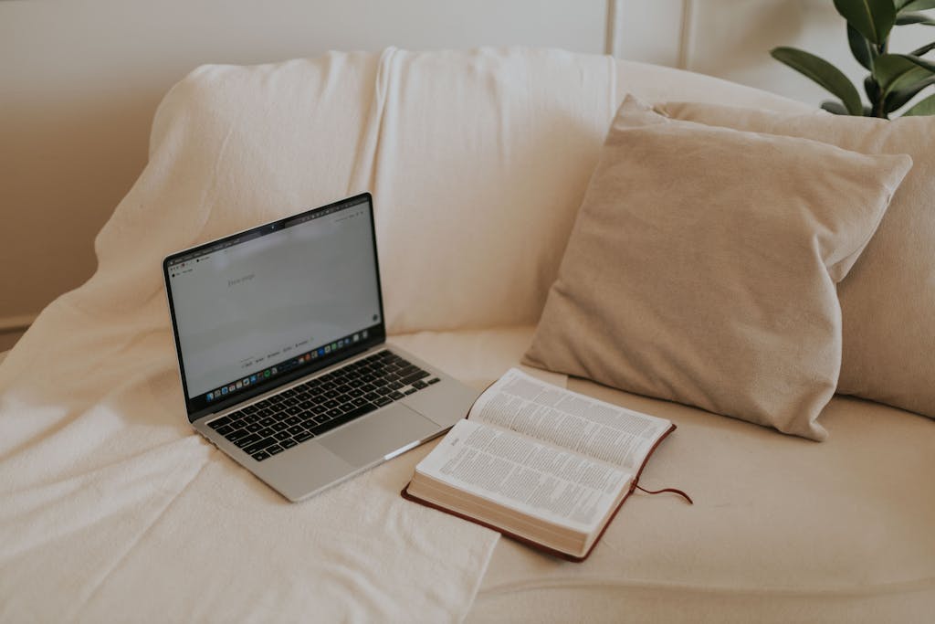 A serene home workspace featuring a laptop and open Bible on a comfortable sofa setting.