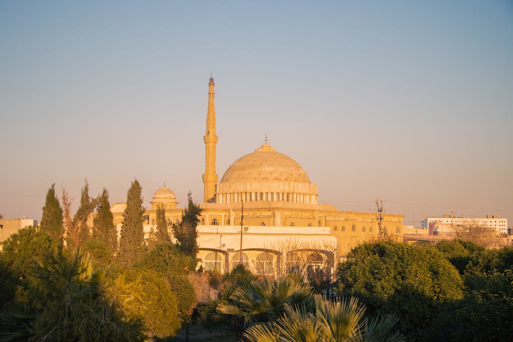 A sunlit mosque in Erbil, Kurdistan Region, Iraq, surrounded by trees.