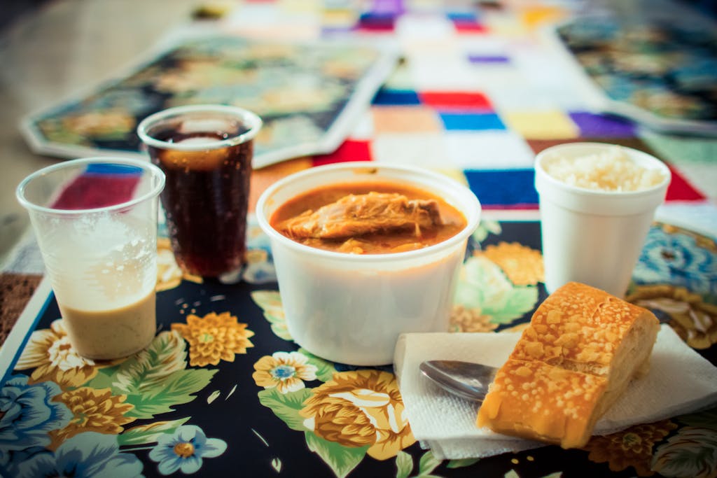A vibrant display of a delicious meal featuring soup, bread, rice, and drinks on a patterned tablecloth.