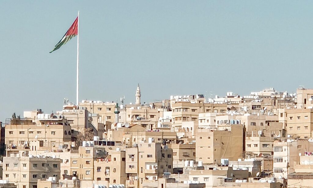 A view of Amman cityscape featuring buildings and the Jordanian flag under a clear sky.