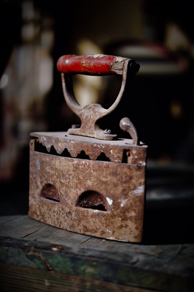 A vintage coal iron with a red handle displayed on a wooden surface, evoking nostalgia.