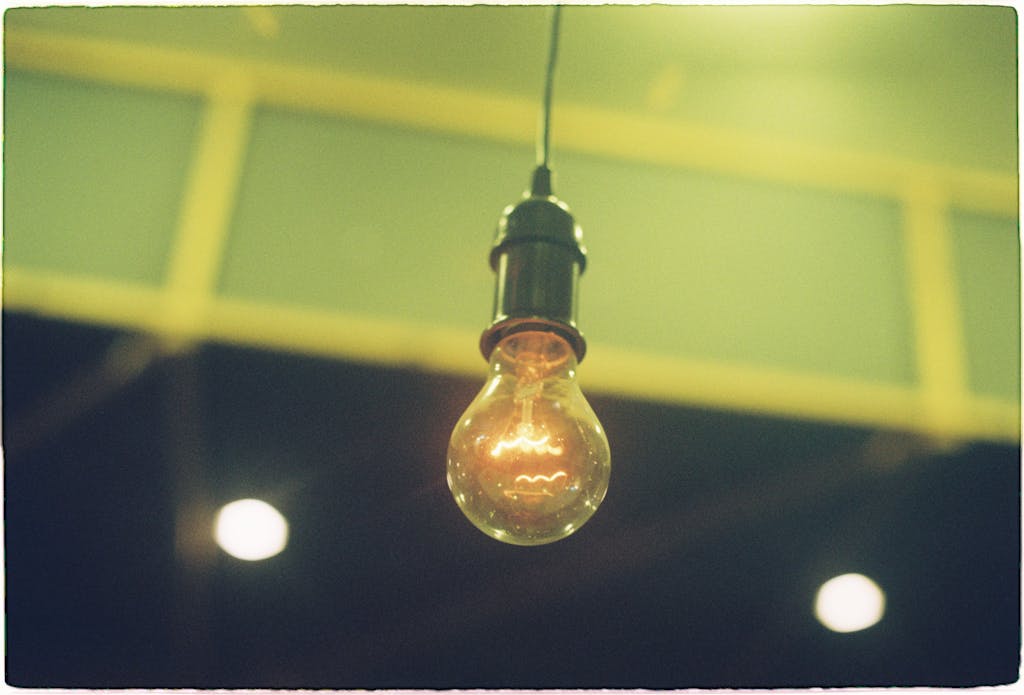 A vintage incandescent light bulb hanging indoors, casting a warm glow.