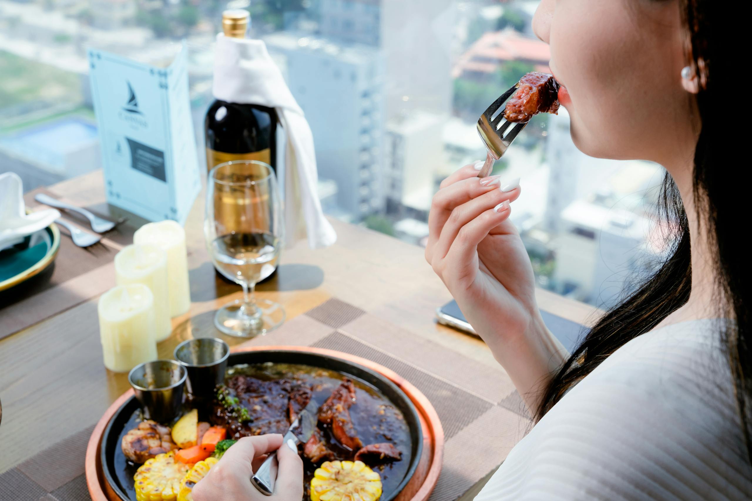 A woman enjoying a fine dining experience with steak and wine in a restaurant setting.