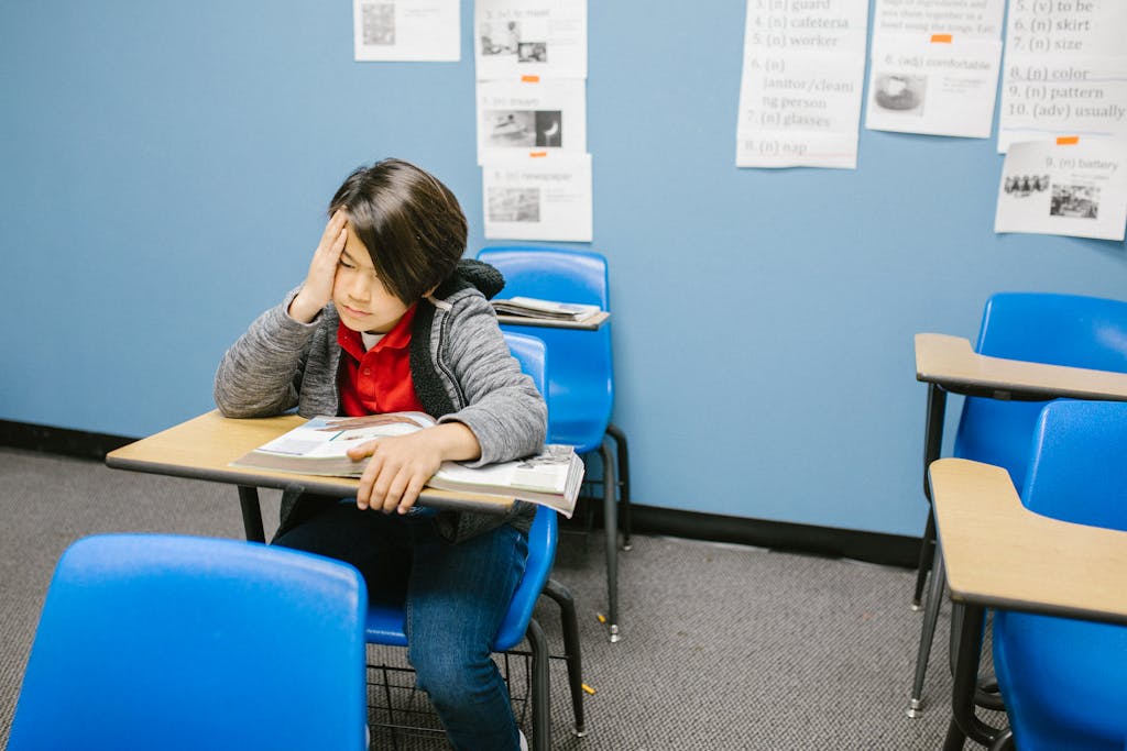 A young student sitting alone in a classroom, looking thoughtful and isolated.