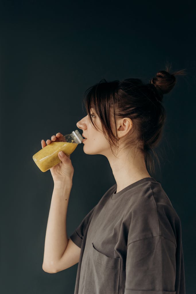 A young woman drinks healthy fruit juice from a bottle in a side view portrait.