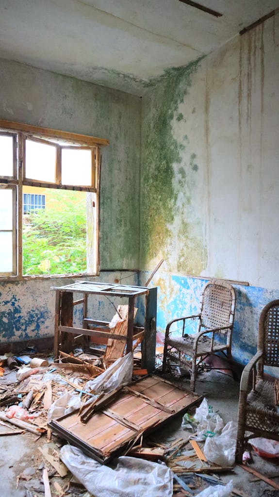Abandoned room with peeling walls, broken furniture, and debris, evoking decay.