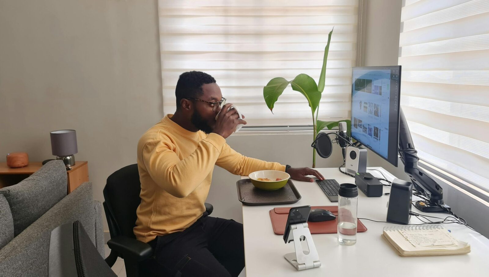 African American man working from a modern home office, drinking while using a computer.