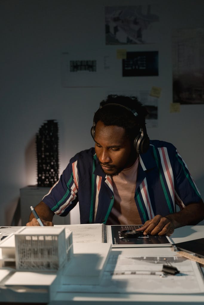 An architect wearing headphones diligently sketching designs at a night-lit workspace.