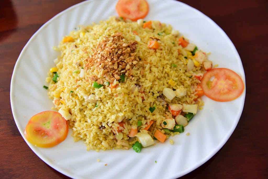 Appetizing vegetarian fried rice garnished with tomatoes and vegetables on a white plate.