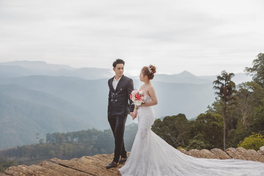 Bride and groom holding hands on a mountain cliff with a stunning view.