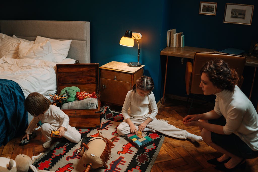 Children engaging with toys in a cozy bedroom, supervised by a nanny. Warm indoor scene.