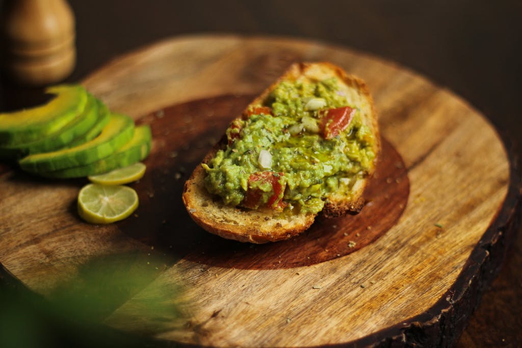 Close-up of avocado toast on a wooden board with sliced avocados, highlighting a gourmet snack.
