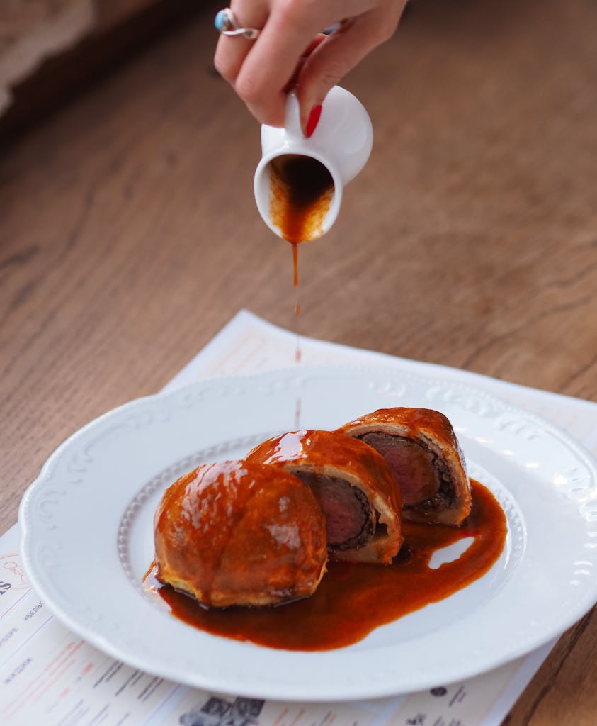 Close-up of beef Wellington with sauce being poured, a delicious gourmet dish.