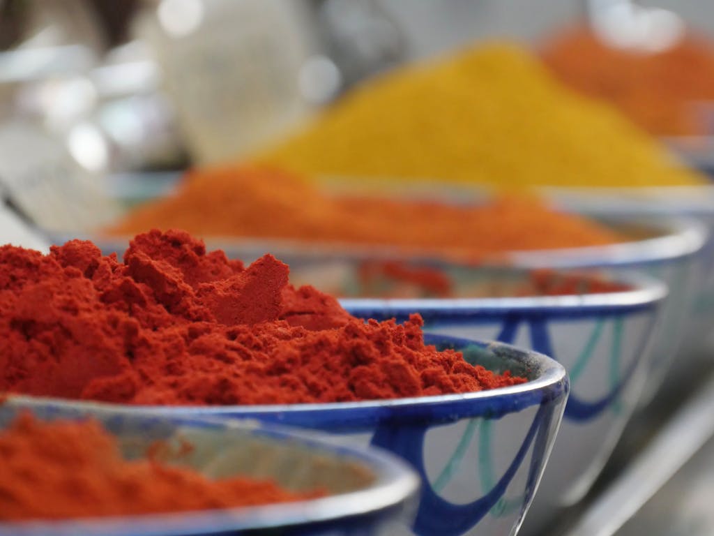 Close-up of colorful spices in bowls at a market, showcasing vibrant hues of red, orange, and yellow.