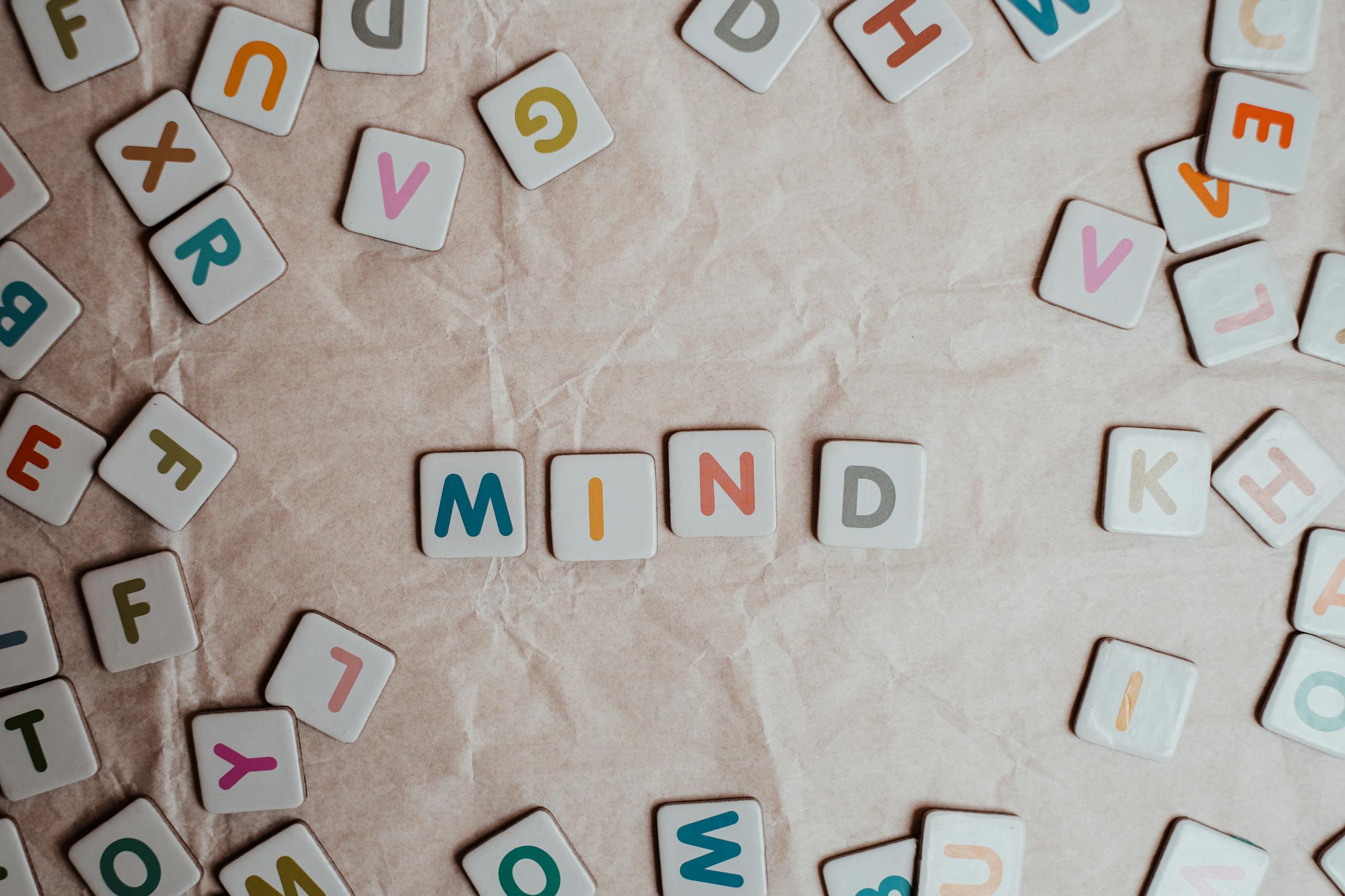 Close-up of scattered letter tiles spelling 'mind' on crumbled paper background.