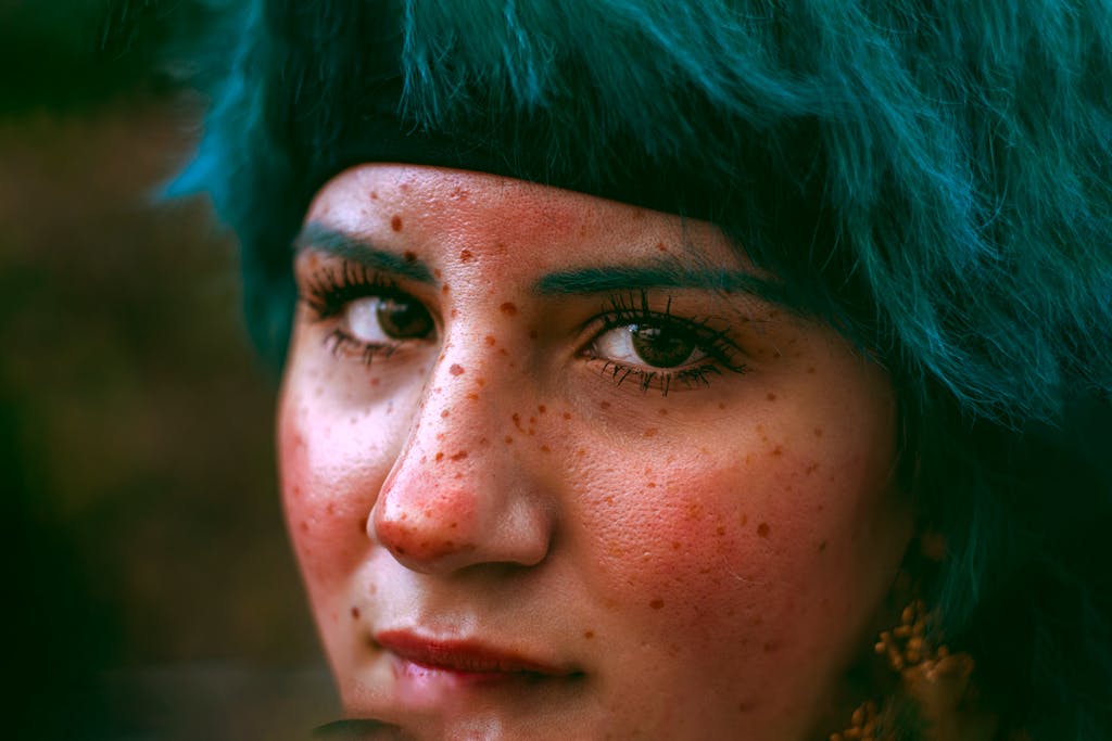Close-up portrait of a woman with freckles and striking blue hair.